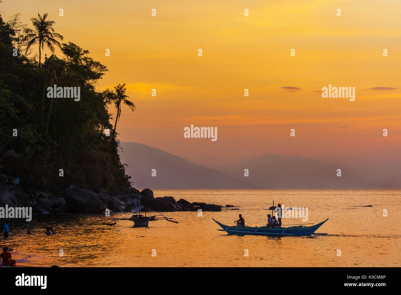 Una canoa outrigger e equipaggio fa il suo modo di riva durante un bel tramonto sulla spiaggia bianca a Puerto Galera, Mindoro Island, Filippine, Sud-est asiatico Foto Stock