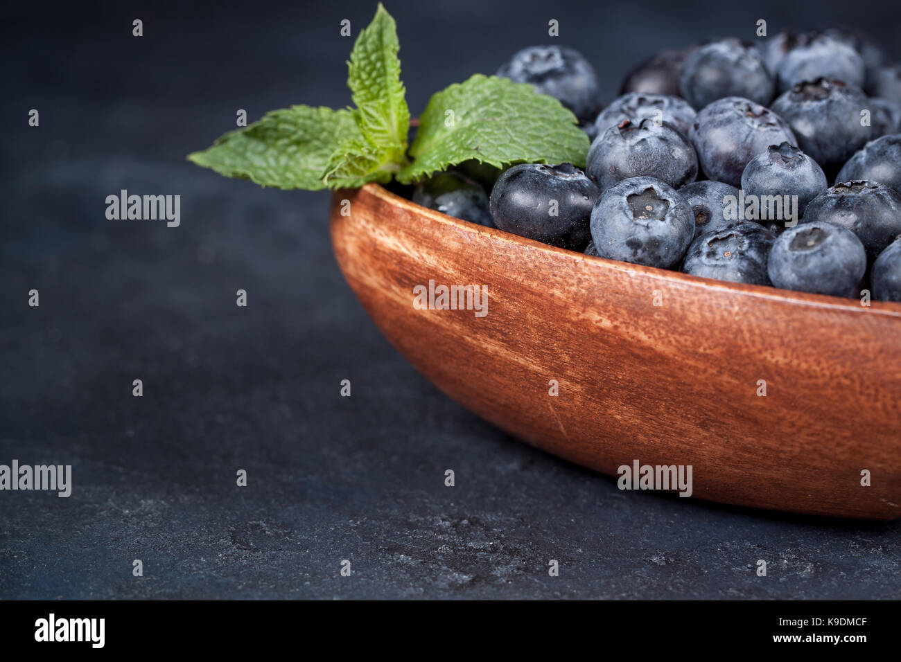 Mirtilli freschi con una foglia di menta in cuore la ciotola sagomata su uno sfondo blu scuro Foto Stock