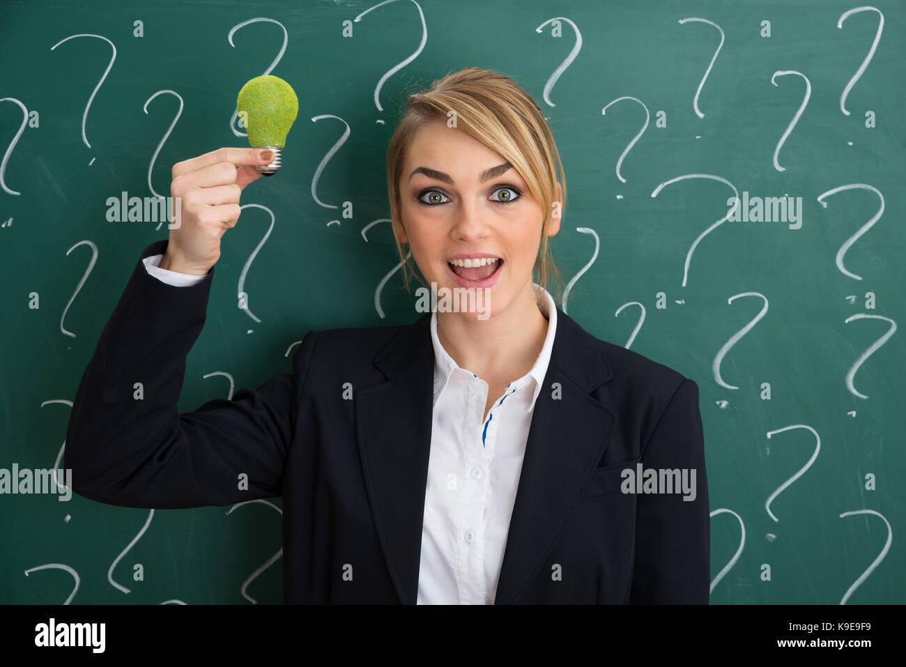 Sorridente giovane imprenditrice di fronte chalkboard holding lampadina ecologica Foto Stock