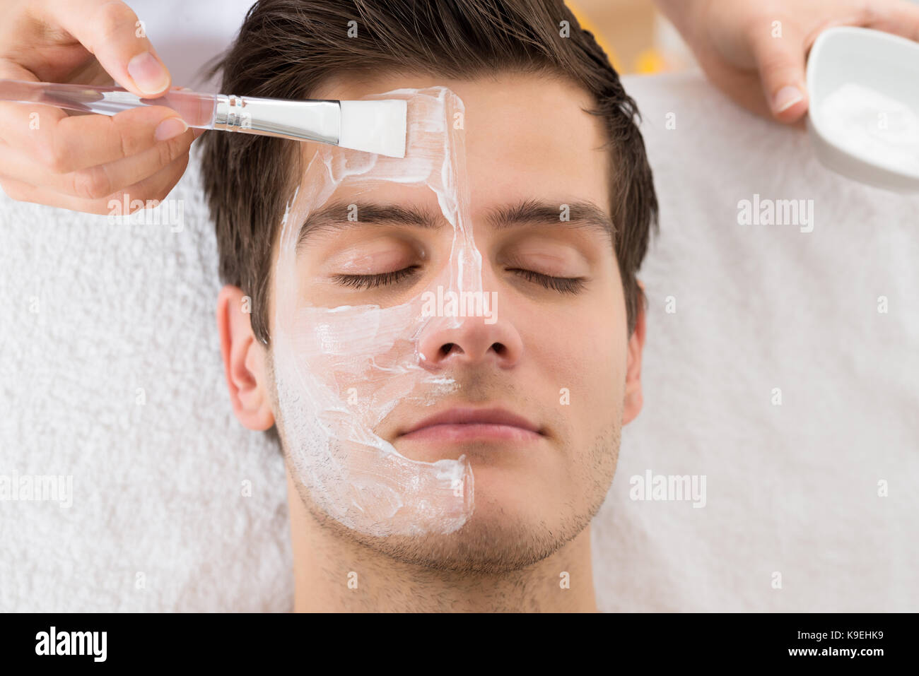 Terapista mani con pennello applicare la maschera per il viso di un giovane uomo in una spa Foto Stock