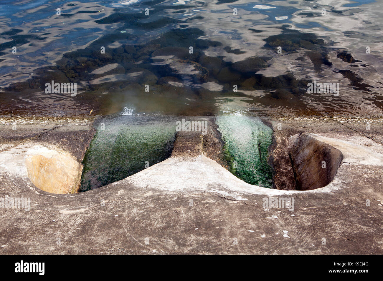 Effluenti inquinanti lo scarico in una baia nell'oceano da un sistema fognario cittadino in una delle più importanti del sud-est del paese asiatico. Melma verde sentieri verso il basso il calcestruzzo faccia Foto Stock