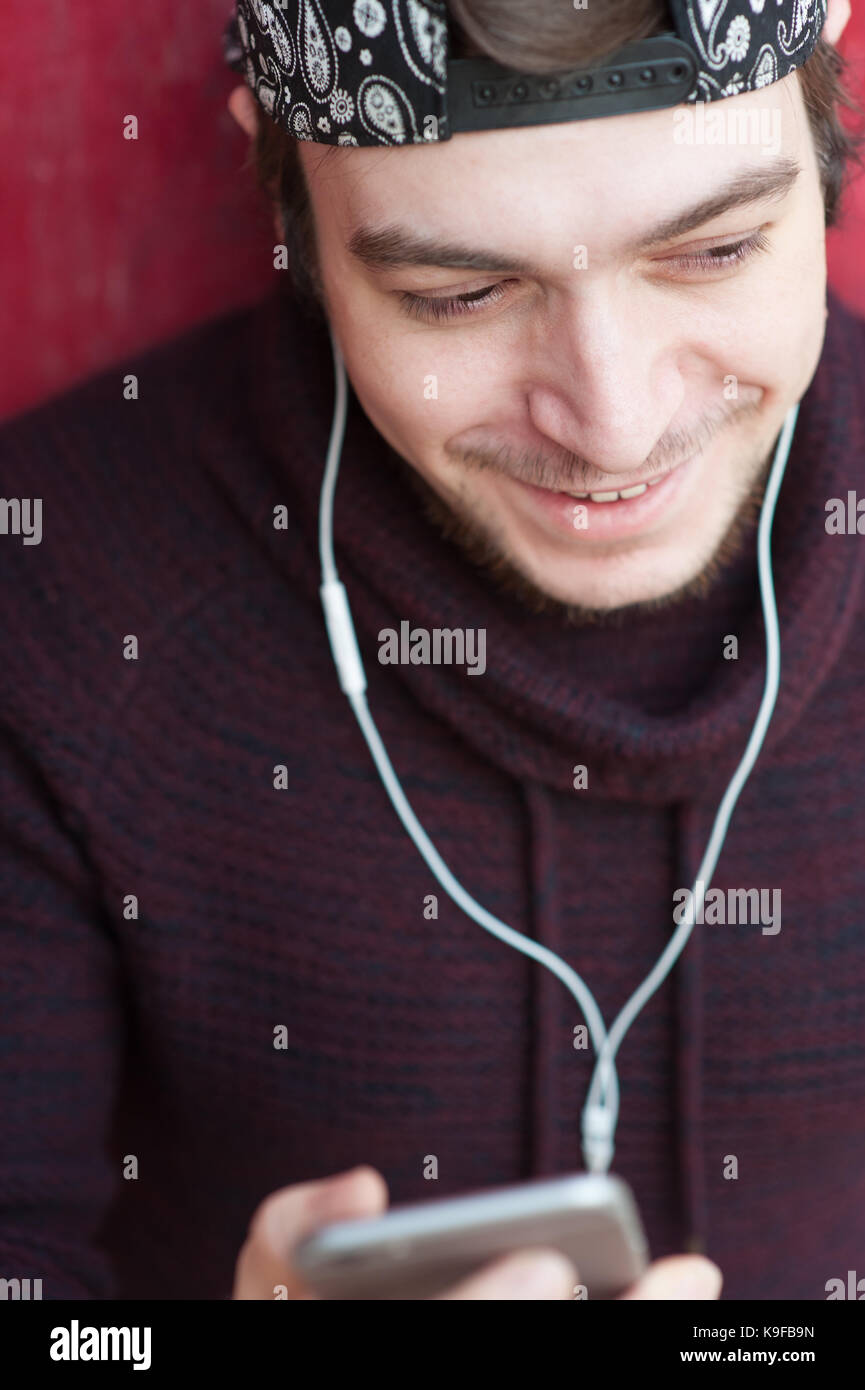 Sorridente bel giovane uomo con la barba che indossa un maglione di lana e  un cappello da baseball con uno smartphone e che indossano le cuffie Foto  stock - Alamy