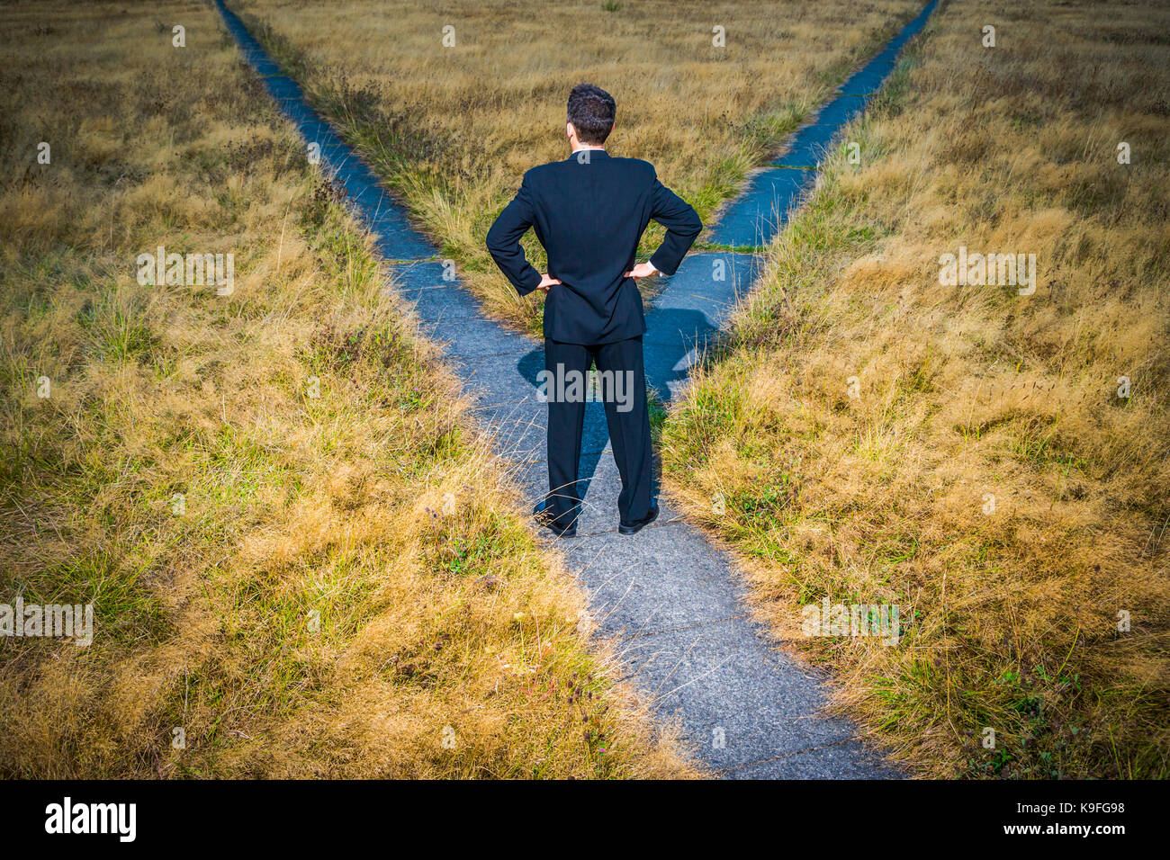 Un uomo in un business suit sorge in una strada trasversale che stanno cercando di capire in che modo andare. Foto Stock