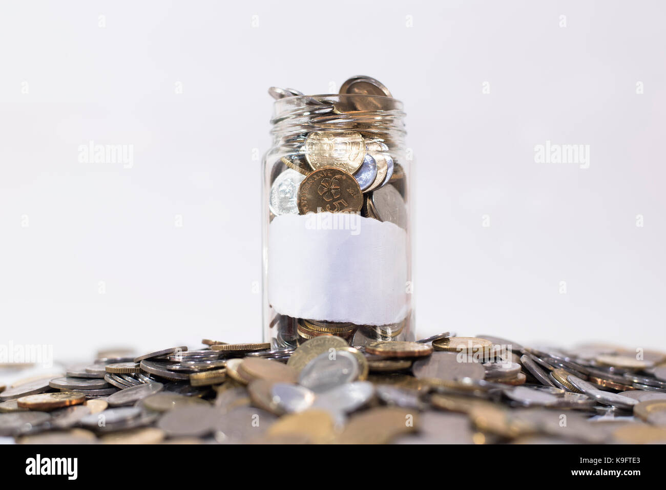 Il vasetto di vetro riempito con monete su un gruppo di monete.attaccato con vuoto carta bianca. isolato su sfondo bianco. concetto finanziario. malaysia valuta Foto Stock