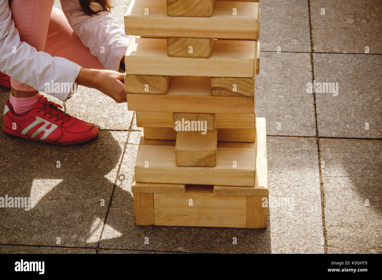 La Ragazza tira fuori un blocco di legno dalla torre Jenga giocando al gioco street. Riproduci jung con una grande e blocchi di legno, i giochi per i bambini. Foto Stock