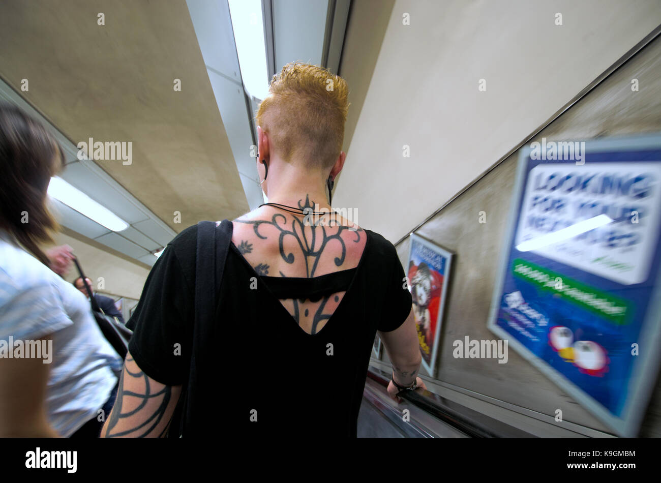 Londra, Inghilterra, Regno Unito. Donna con tatuaggi su una scala mobile verso il basso sulla metropolitana Foto Stock