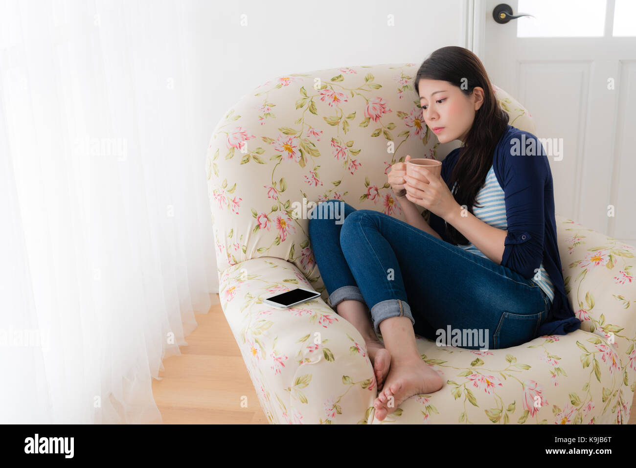 Piacevole bellezza lady coppa di ritegno bere seduti sul divano confortevole sedia e guardando il telefono cellulare aspetta avente un buon messaggio. Foto Stock
