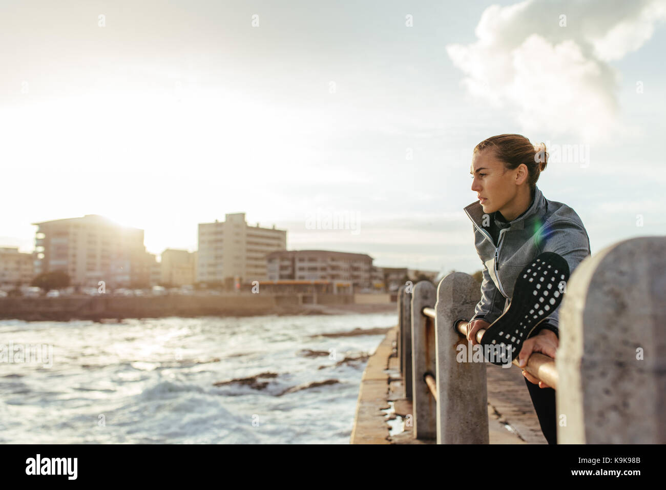 Giovane donna sana che si allunga le gambe su una ringhiera sulla strada di mare. fitness donna che avverte sulla strada in riva al mare. Foto Stock
