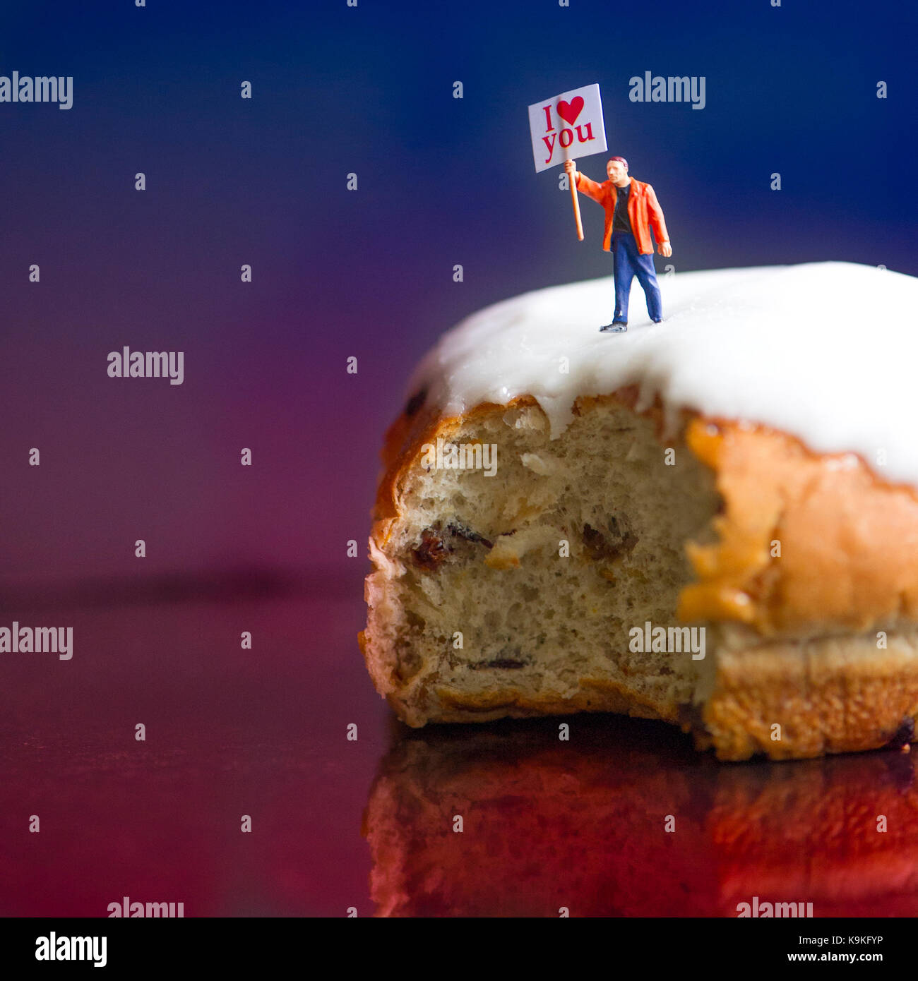 "Ti amo oltre le ciambelle glassate' - piccolo uomo si arrampica sulla cima di un appiccicoso iced bun tenendo un cartello proclamare "ti amo". Foto Stock