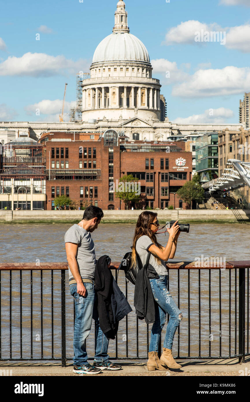 Coppia giovane appoggiata contro una recinzione dal fiume Tamigi in bankside southwark Londra indossando cime grigio e blu jeans denim di scattare fotografie con una Foto Stock