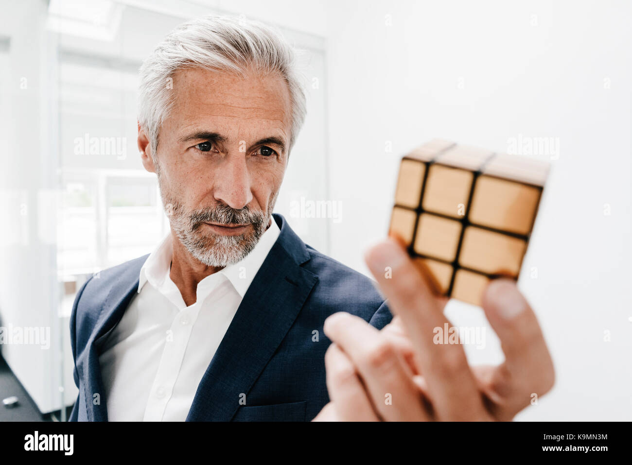 Imprenditore maturo in office esaminando il cubo di Rubik Foto Stock