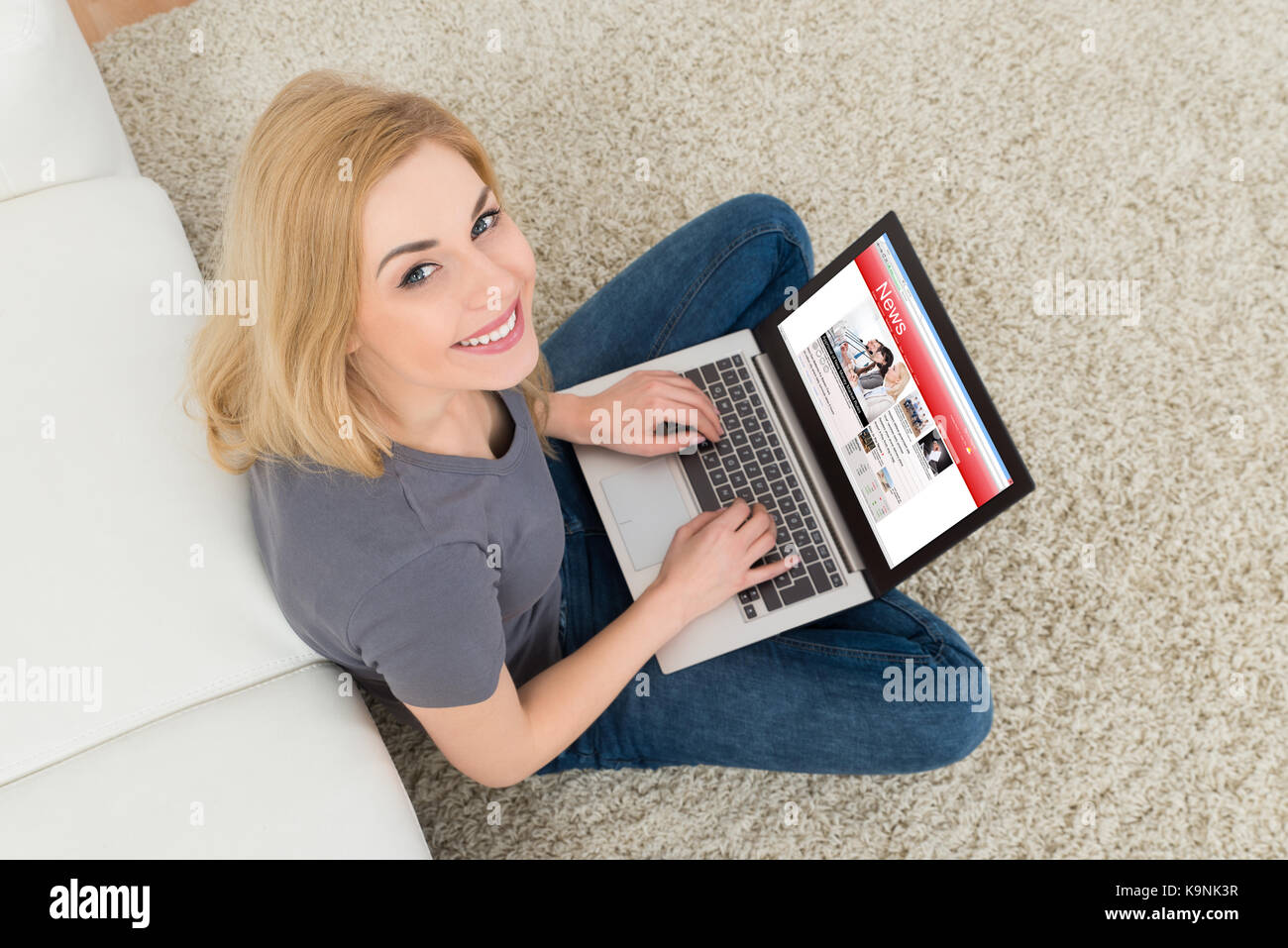 Angolo di alta vista della giovane donna felice con notizie su laptop Foto Stock