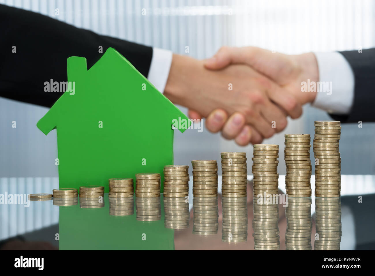 Gli imprenditori agitando la mano nella parte anteriore di una pila di monete e green house modello Foto Stock