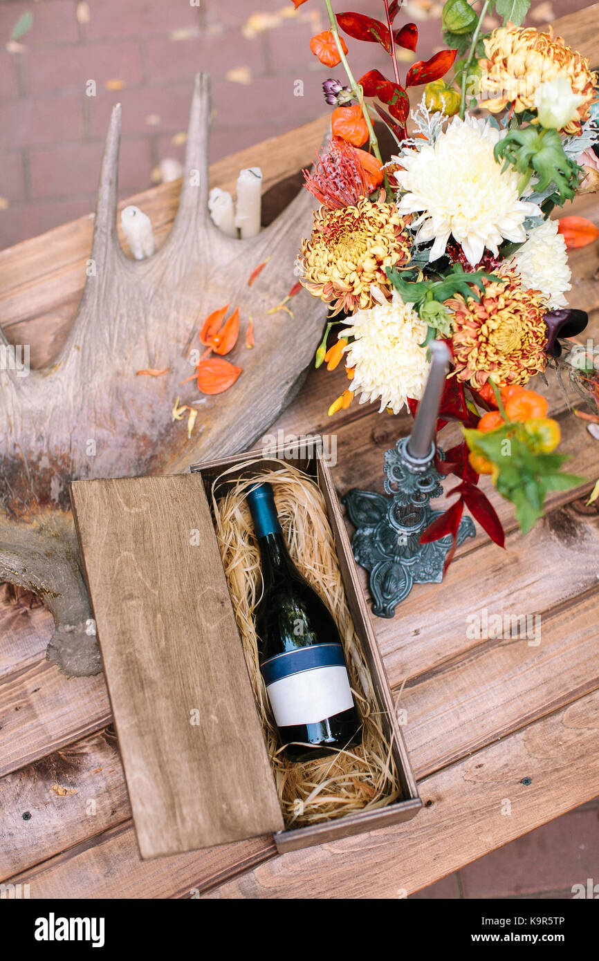 Arte, disponendo, alcol concetto. sul tavolo di legno vi è perfetta ancora in vita con bottiglia di vino in una speciale scatola, gran corno di alci, candela in grigio di vecchi titolare e il mazzetto di chrisantemums Foto Stock