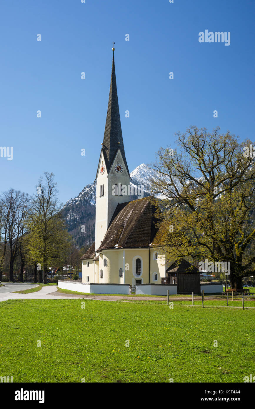 La chiesa di San Leonardo al Lago schliersee di fronte montagne innevate e germinazione Foglie sugli alberi nella luce del sole primaverile, Baviera Germania Foto Stock