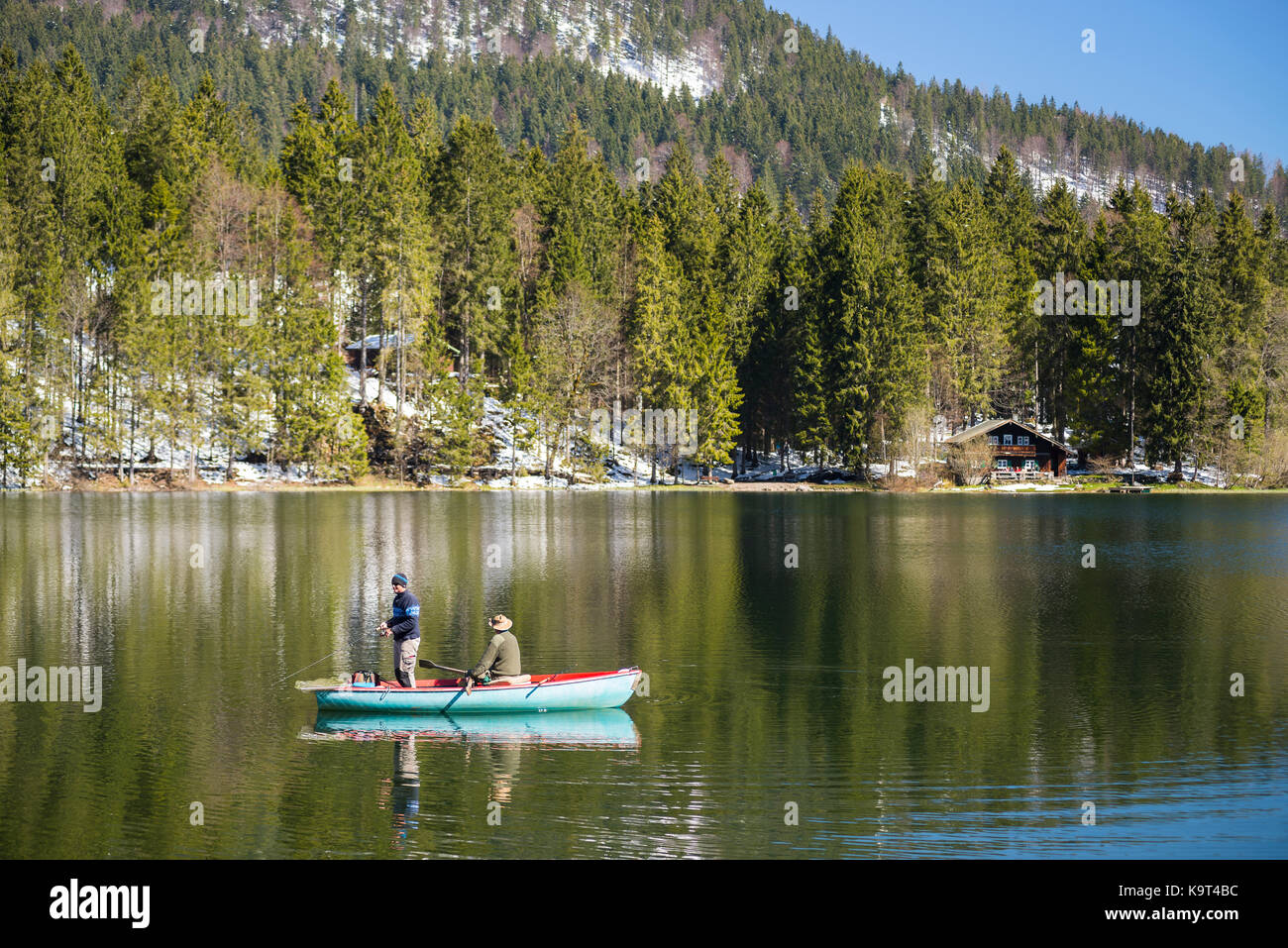 Due pescatori in barca a remi sul lago spitzingsee di fronte montagne innevate e foreste di montagna in primavera, Baviera, Germania Foto Stock