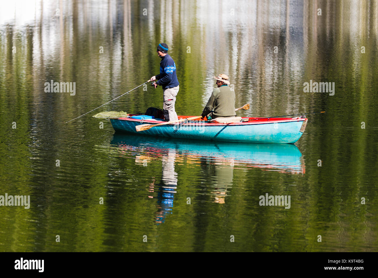 Due pescatori in barca a remi sul lago spitzingsee di fronte montagne innevate e foreste di montagna in primavera, Baviera, Germania Foto Stock