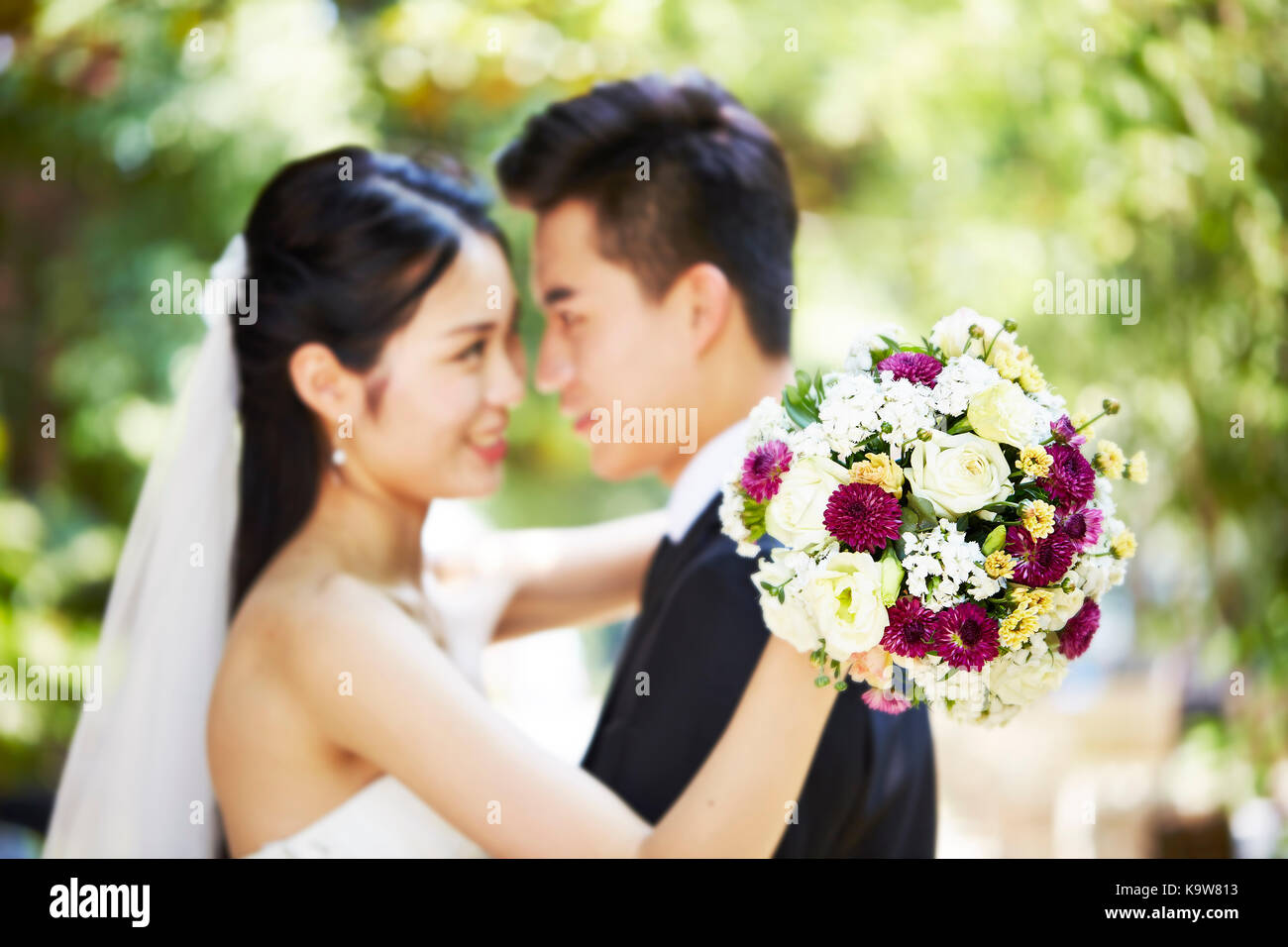 Giovani asiatici coppia di novelli sposi che abbraccia ogni altro durante la cerimonia di nozze, concentrarsi sul mazzo di fiori. Foto Stock