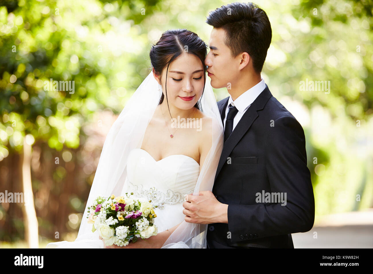 Giovani asiatici groom kissing sposa all'aperto durante la cerimonia nuziale. Foto Stock