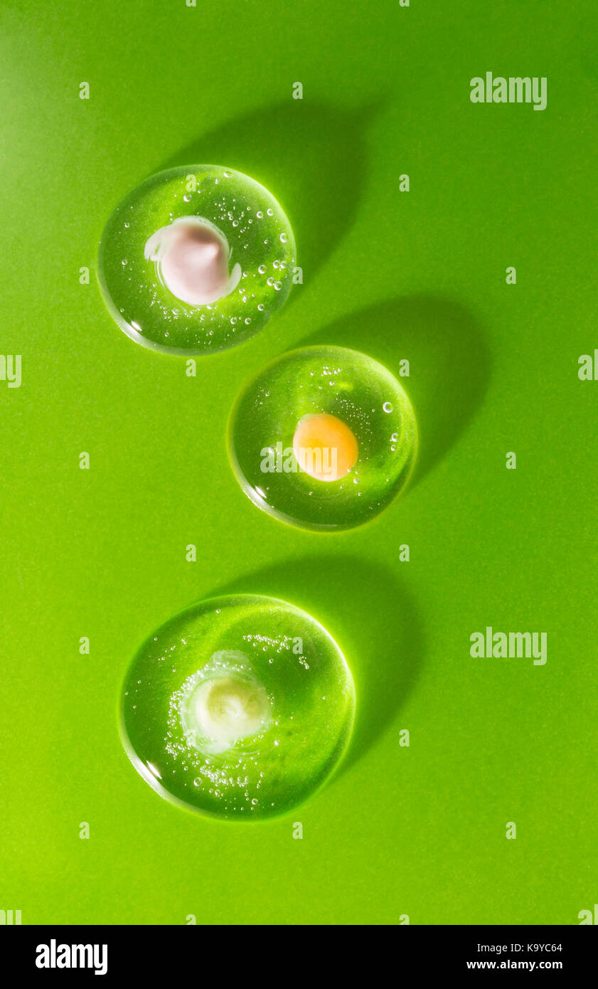 Tre gocce di cosmetico clear gel con varie creme su uno sfondo verde. Il concetto di compatibilità biologica dei prodotti con la pelle umana Foto Stock