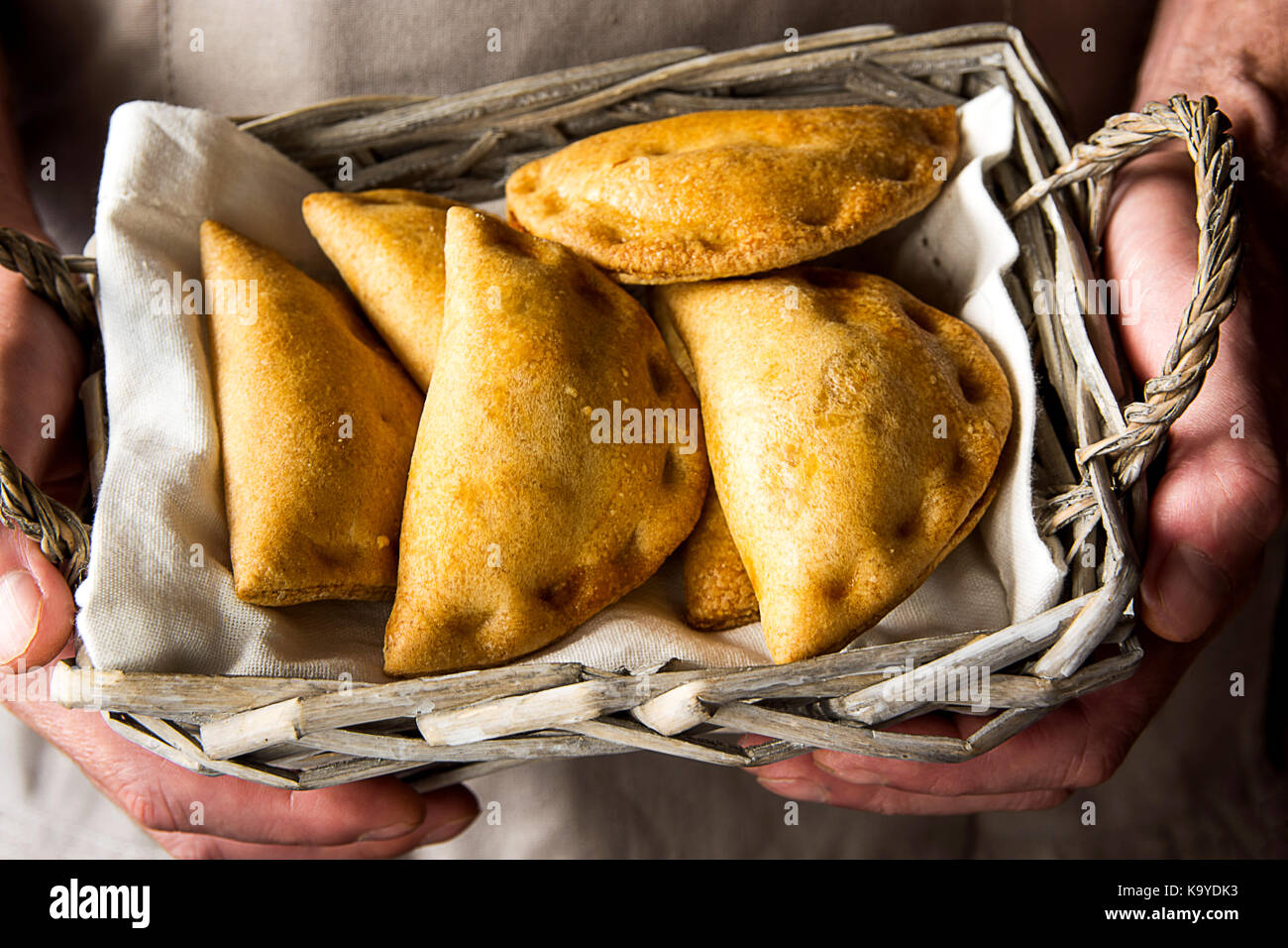 L uomo lo chef tenendo in mano un cesto di vimini con appena sfornato empanadas vegetariane fatturato torte con verdure formaggio in salsa di pomodoro. autentico kinf Foto Stock
