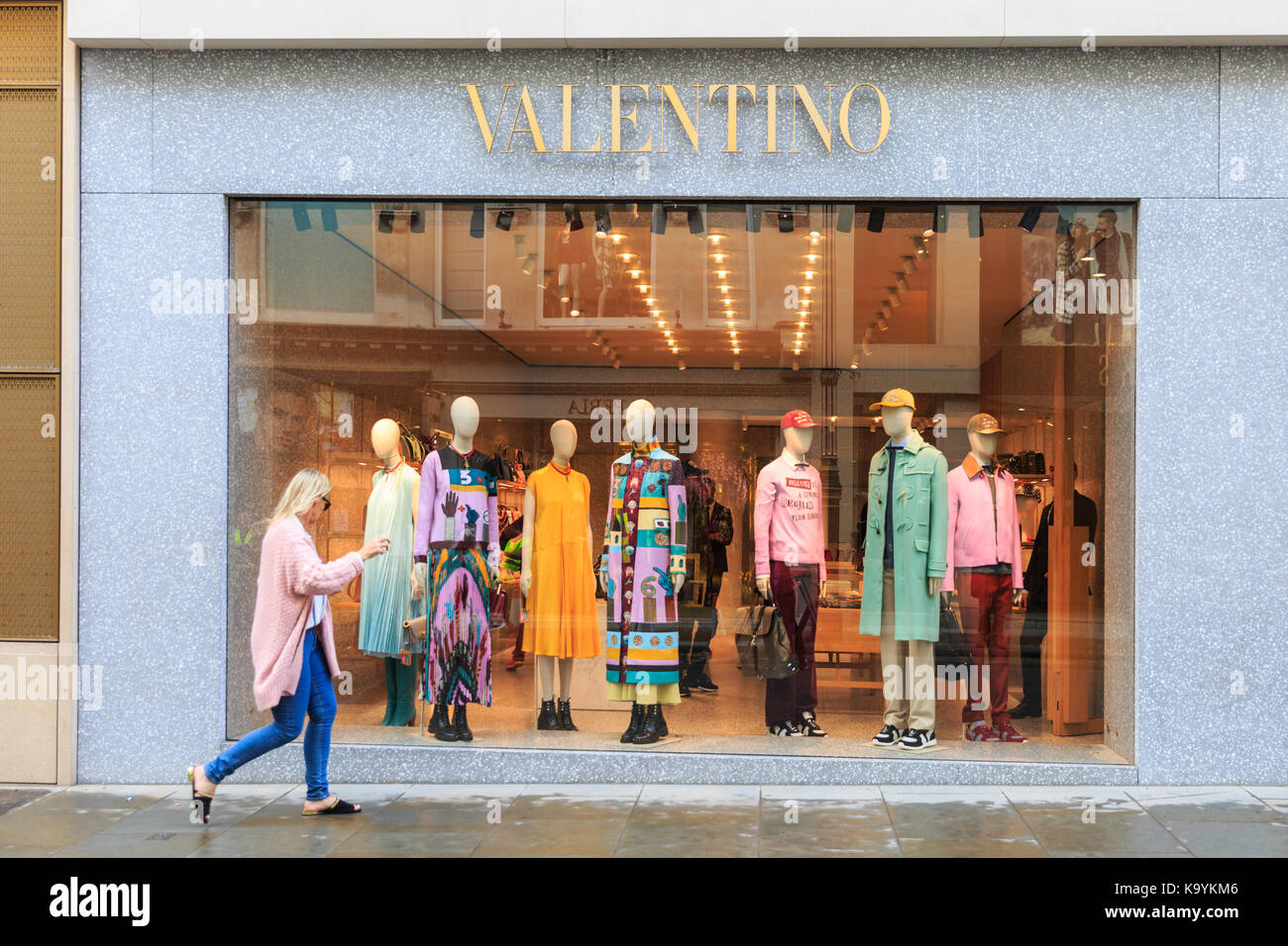 Esterno vetrina, donna camminando passato designer di Valentino fashion shop in bond street a Londra, Inghilterra Foto Stock