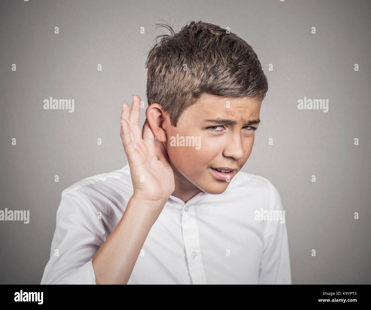 Closeup ritratto infelice di udito collocando man mano sull'orecchio chiedendo a qualcuno di parlare, ascoltare le cattive notizie isolato muro grigio Sfondo. negativ Foto Stock