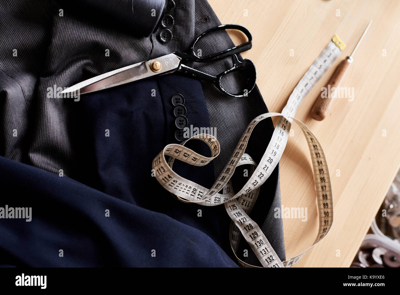 Close-up shot di due classiche giacche, forbici, nastro di misurazione e awl giacente sul piano di lavoro a cucire atelier Foto Stock