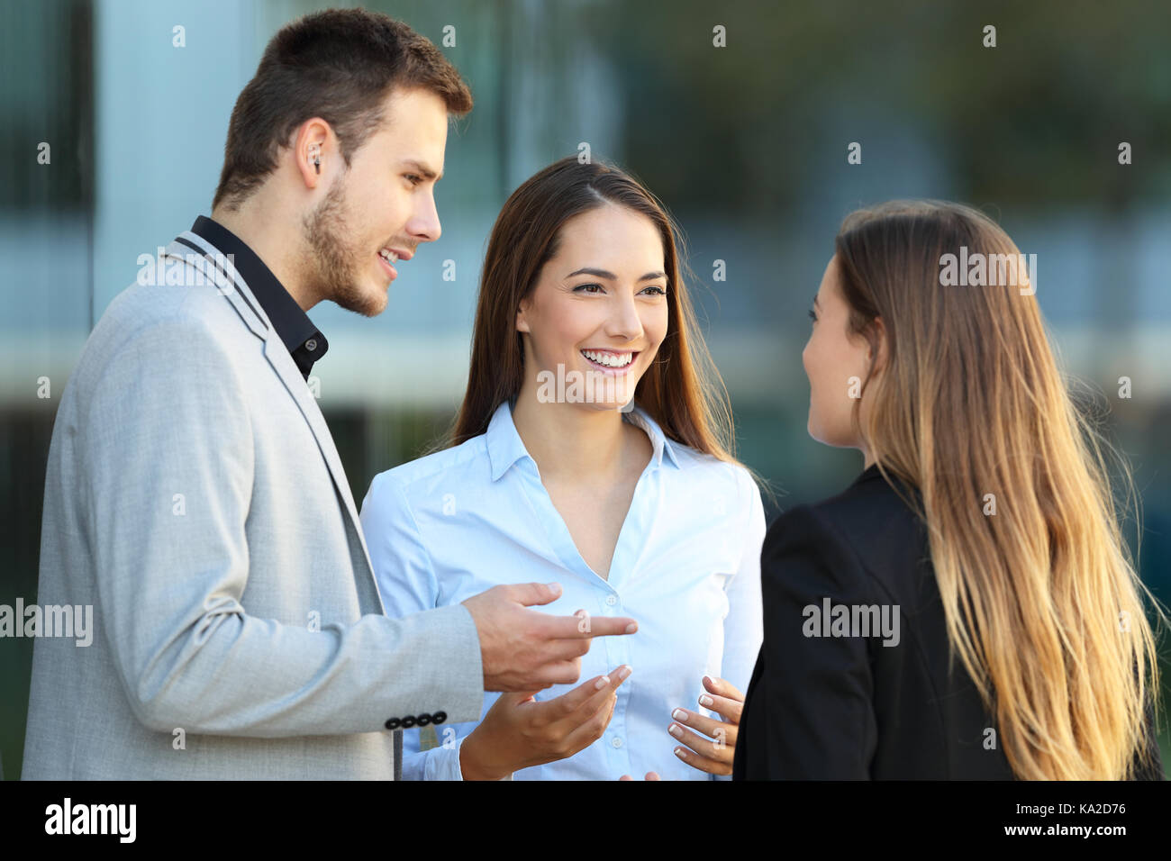 Tre dirigenti felice di parlare in piedi sulla strada con un edificio di uffici in background Foto Stock