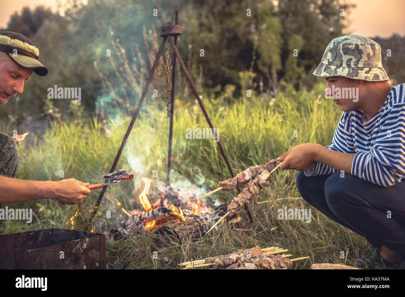 La gente di cottura barbecue all'aperto sul fuoco in summer camp Foto Stock