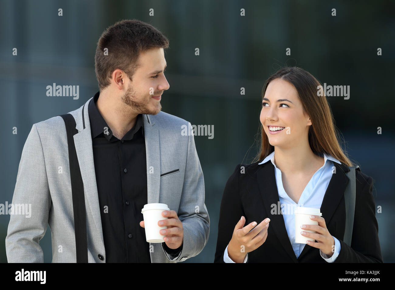 Vista frontale di una coppia felice dei dirigenti a camminare e parlare in strada con un edificio di uffici in background Foto Stock
