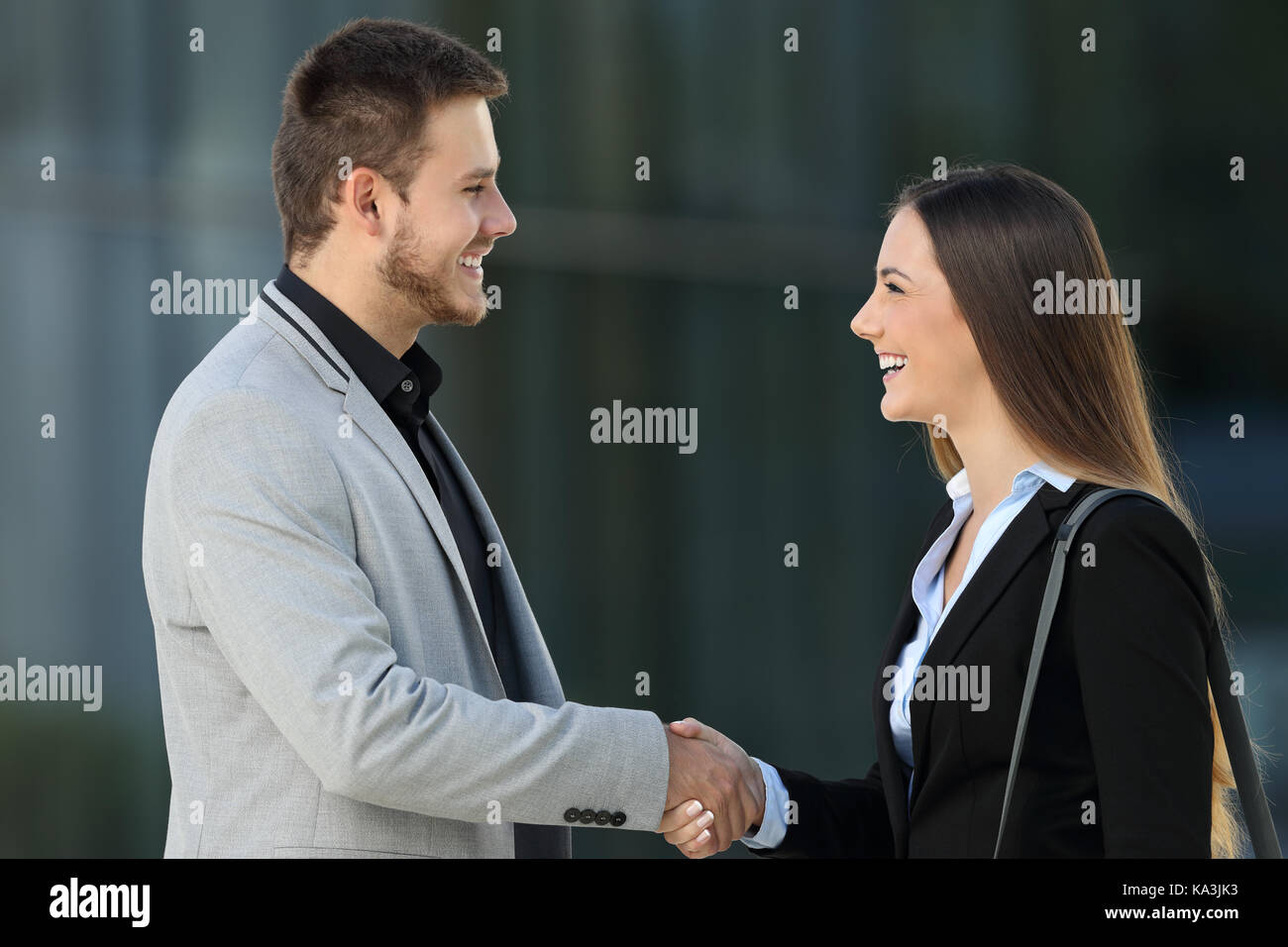 Vista laterale di due dirigenti di felice incontro e lo handshaking sulla strada con un edificio di uffici in background Foto Stock