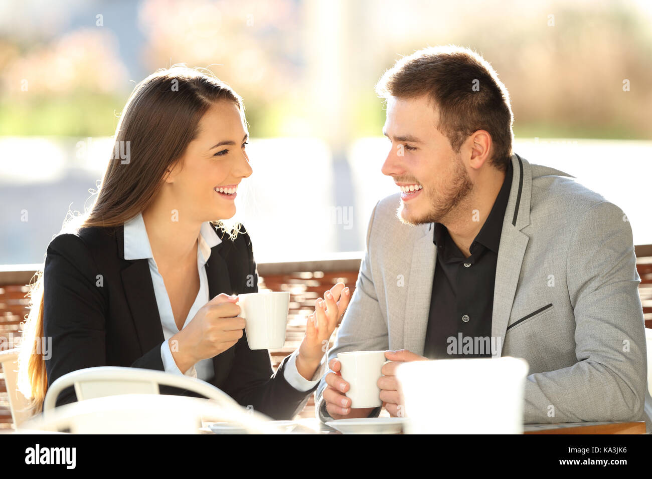 Due dirigenti di parlare durante una pausa caffè seduti in un bar terrazza con una retroilluminazione a caldo Foto Stock