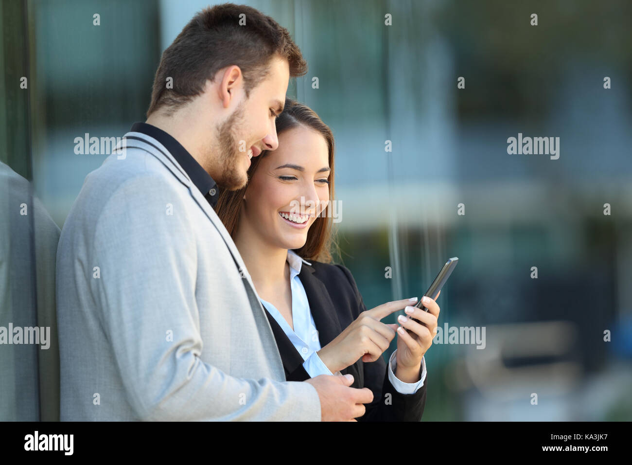 Due dirigenti utilizzando un telefono cellulare appoggiato su di un edificio aziendale sulla strada Foto Stock