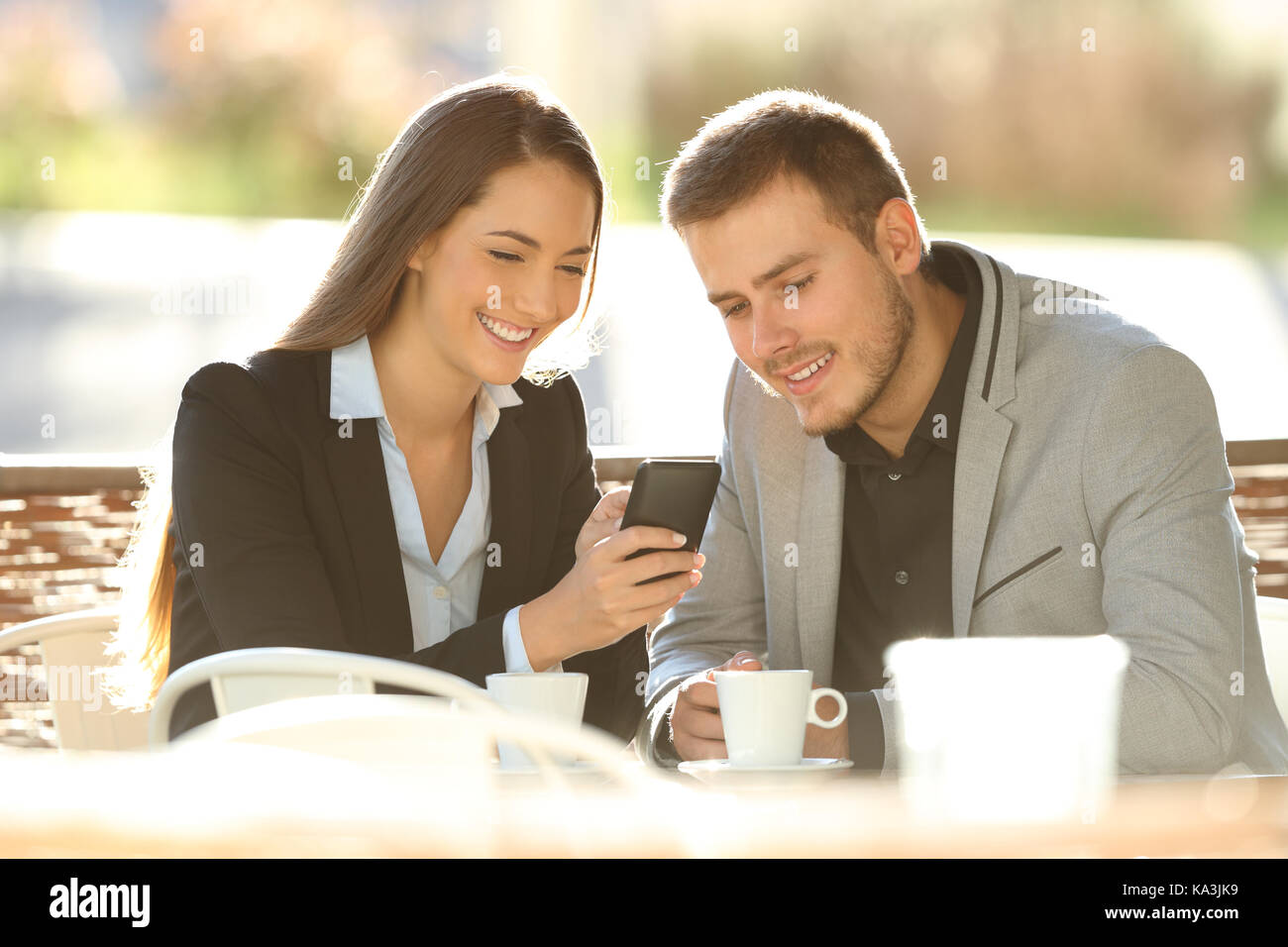 Due dirigenti felice utilizzando uno smart phone seduta in una terrazza ristorante con una calda luce in background Foto Stock