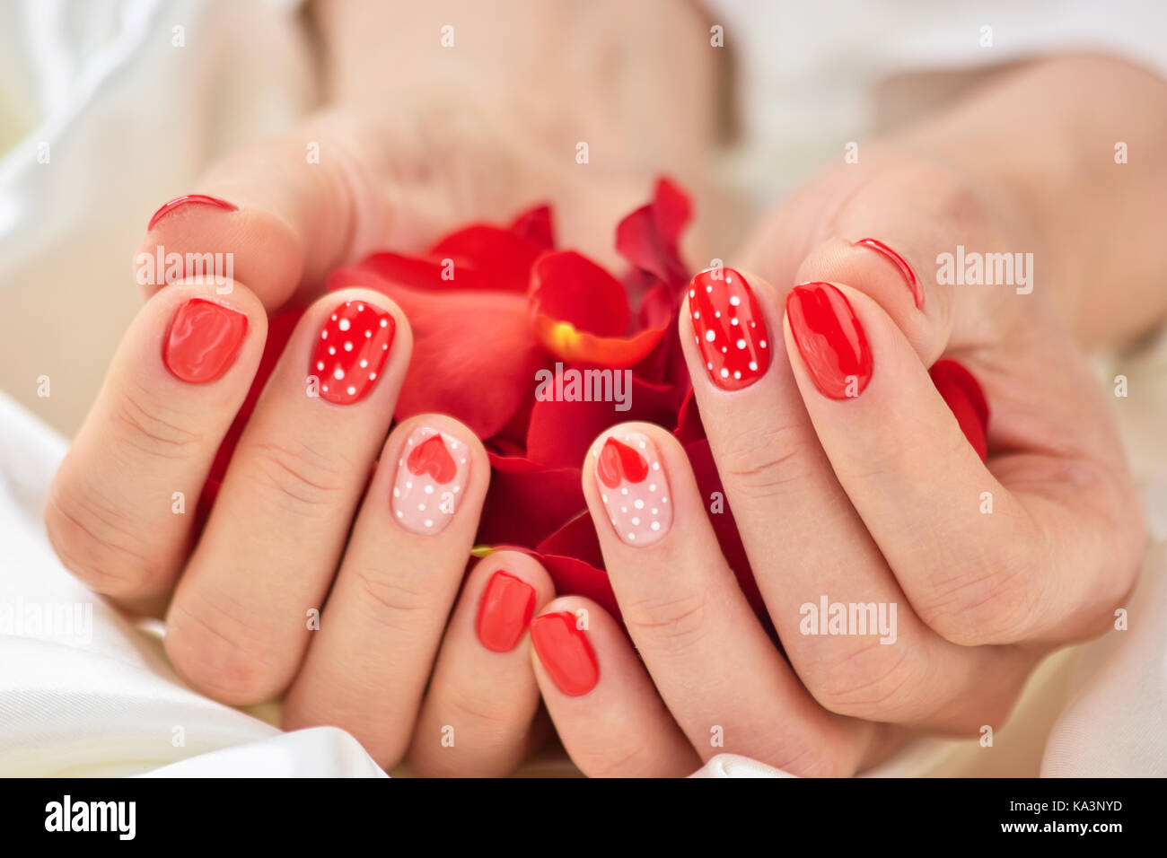 Romantico rosso manicure e petali. Mani belle con perfetta rosso manicure modellato sulle unghie trattate tenendo rose petali di fiori. concettuale romanticismo Foto Stock