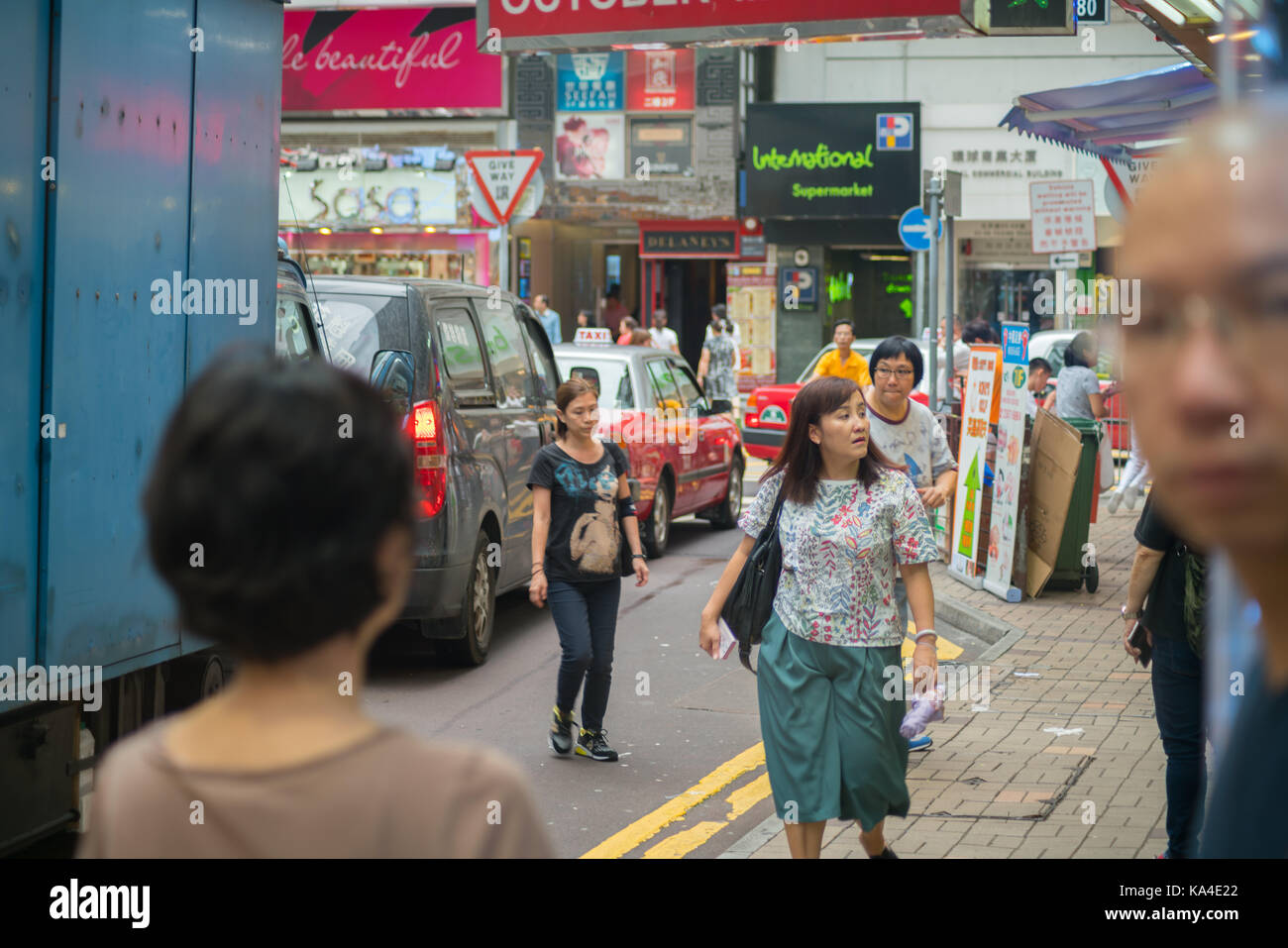 Hong kong, asia - agosto 2, 2017; alcune persone in parte al di fuori del telaio e la messa a fuoco, automobili, gli edifici e i segni nella trafficata strada movimentata scena tipicamente asiatici in Foto Stock
