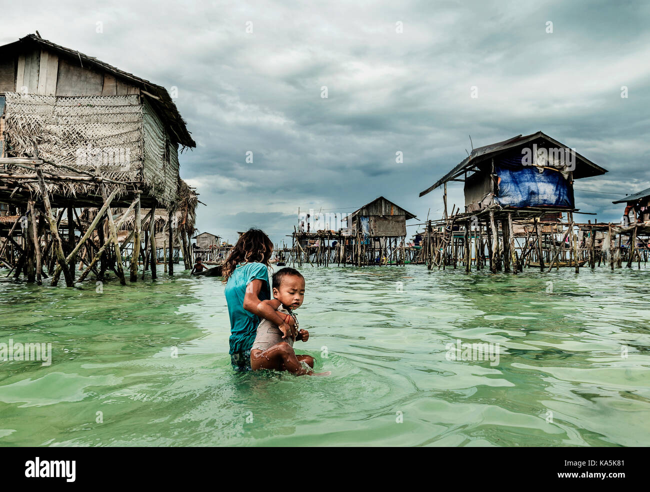 Bambina che porta il suo fratello a casa in Semporna villaggio sul mare, Malaysia Foto Stock