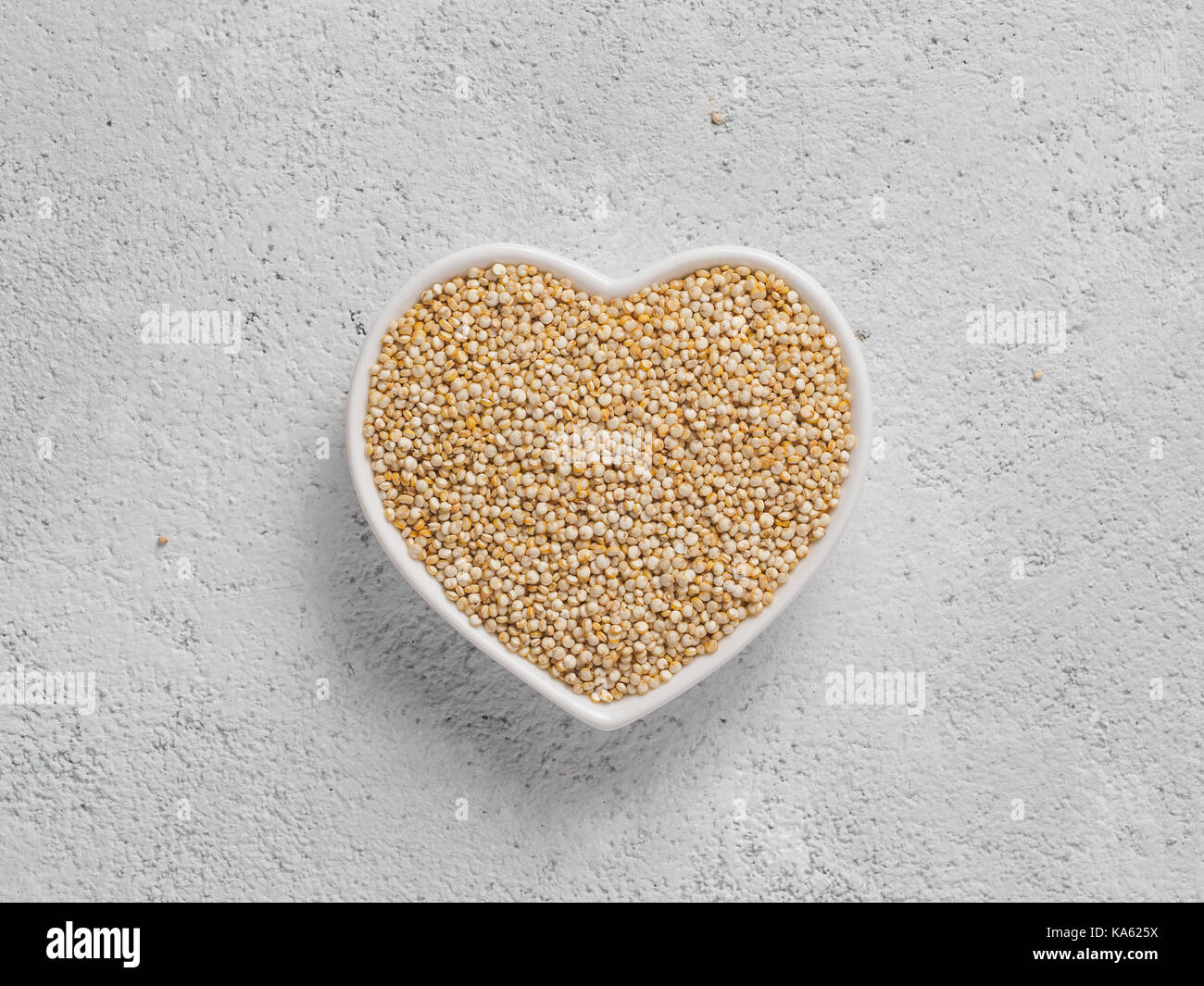 La quinoa nel cuore a forma di ciotola sul cemento grigio Sfondo. Senza glutine di grano antico per una sana dieta. Io amo la quinoa concetto. Copia dello spazio. Foto Stock