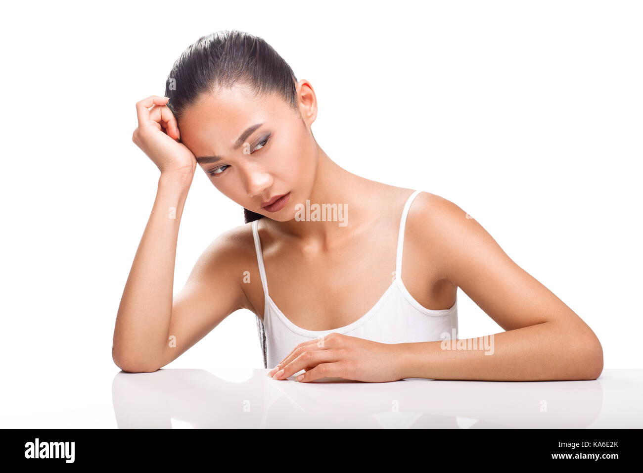Giovane donna asiatica seduta a tavola mettendo la testa sul braccio e sulla triste guardando lontano. ragazza expressesion malattia, situazione stressante, guai. mezzo corpo portra Foto Stock