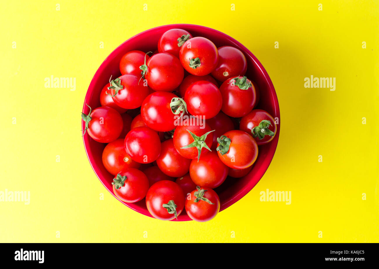 Grappolo di pomodori ciliegia in una ciotola su sfondo giallo Foto Stock