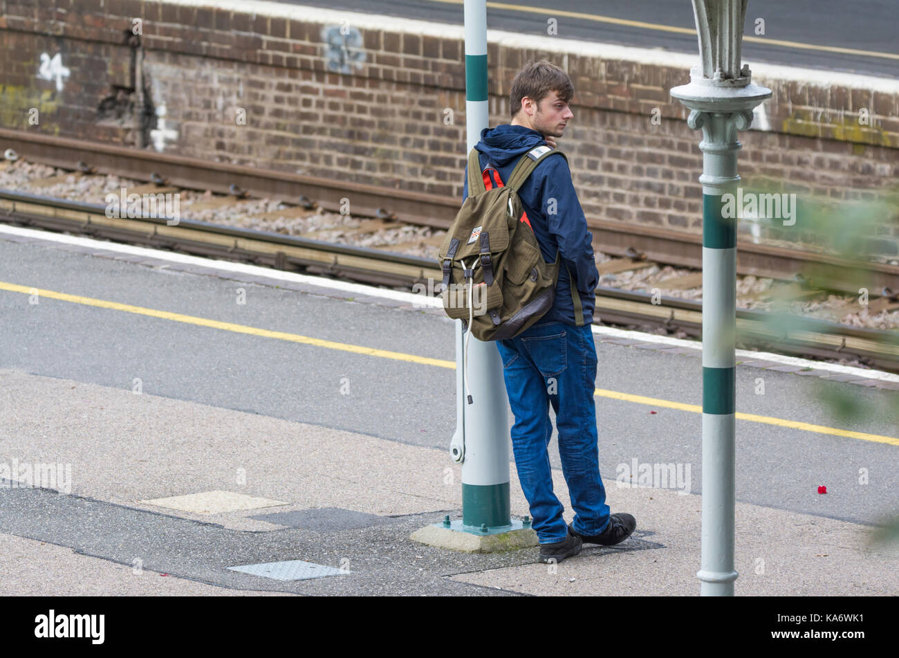 Uomo in piedi su una piattaforma del treno in attesa di un treno in un British railway station in Inghilterra, Regno Unito. Foto Stock