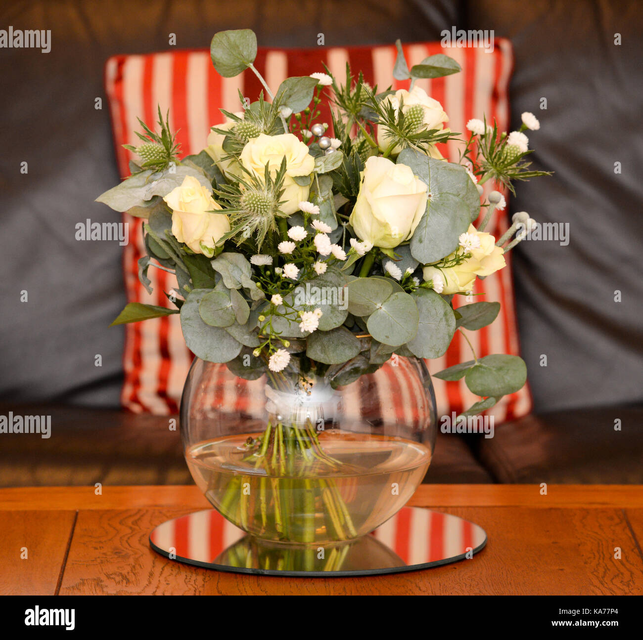 Bouquet di fiori bianchi e rose in un vaso di vetro vaso con una a strisce rosse cuscino dietro. Foto Stock