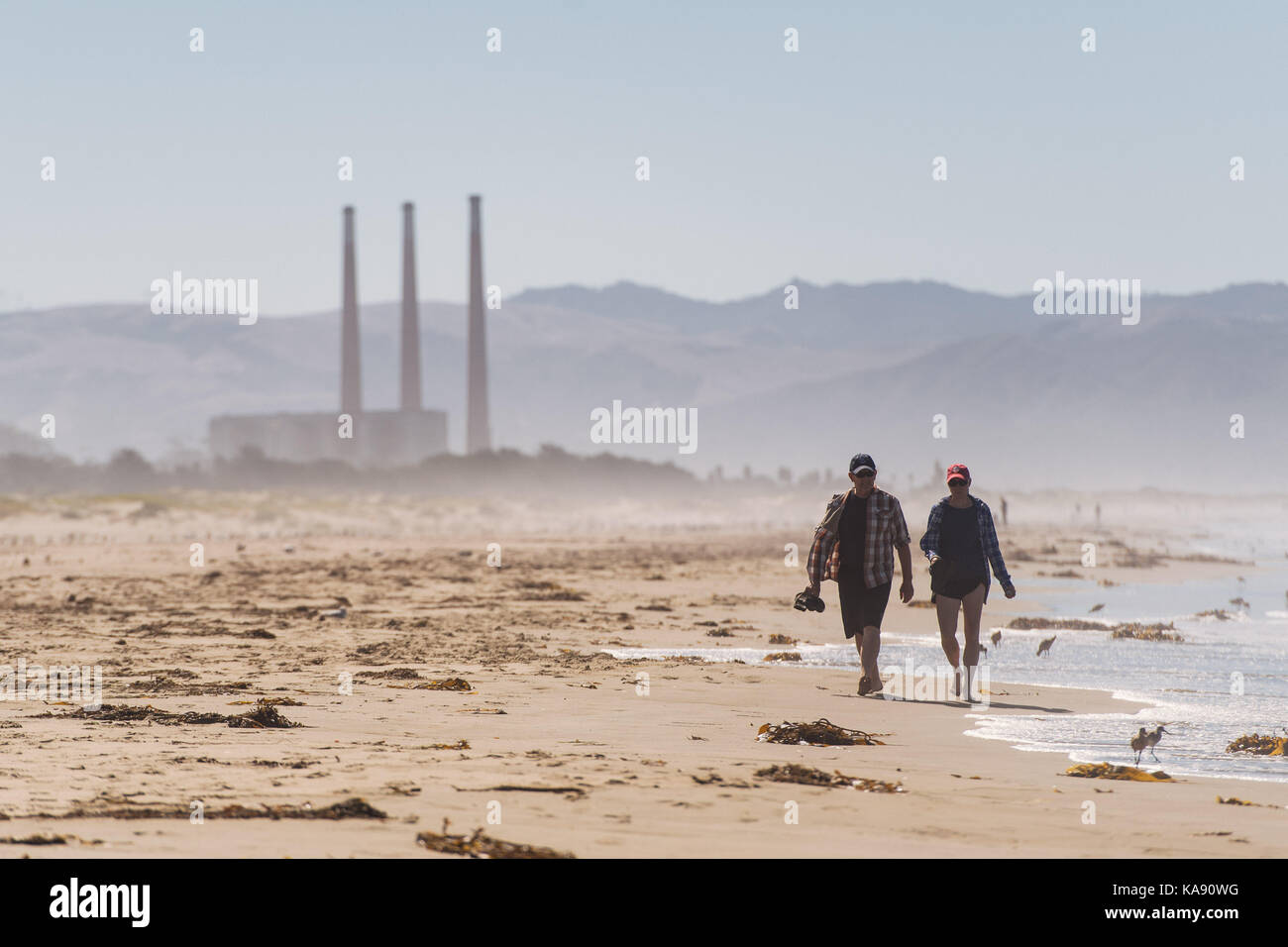 Due persone a piedi lungo Morro Strand State Beach, con Morro Bay mutuo acqua impianto di alimentazione in background, vicino a Morro Bay e Cayucos, California, US Foto Stock