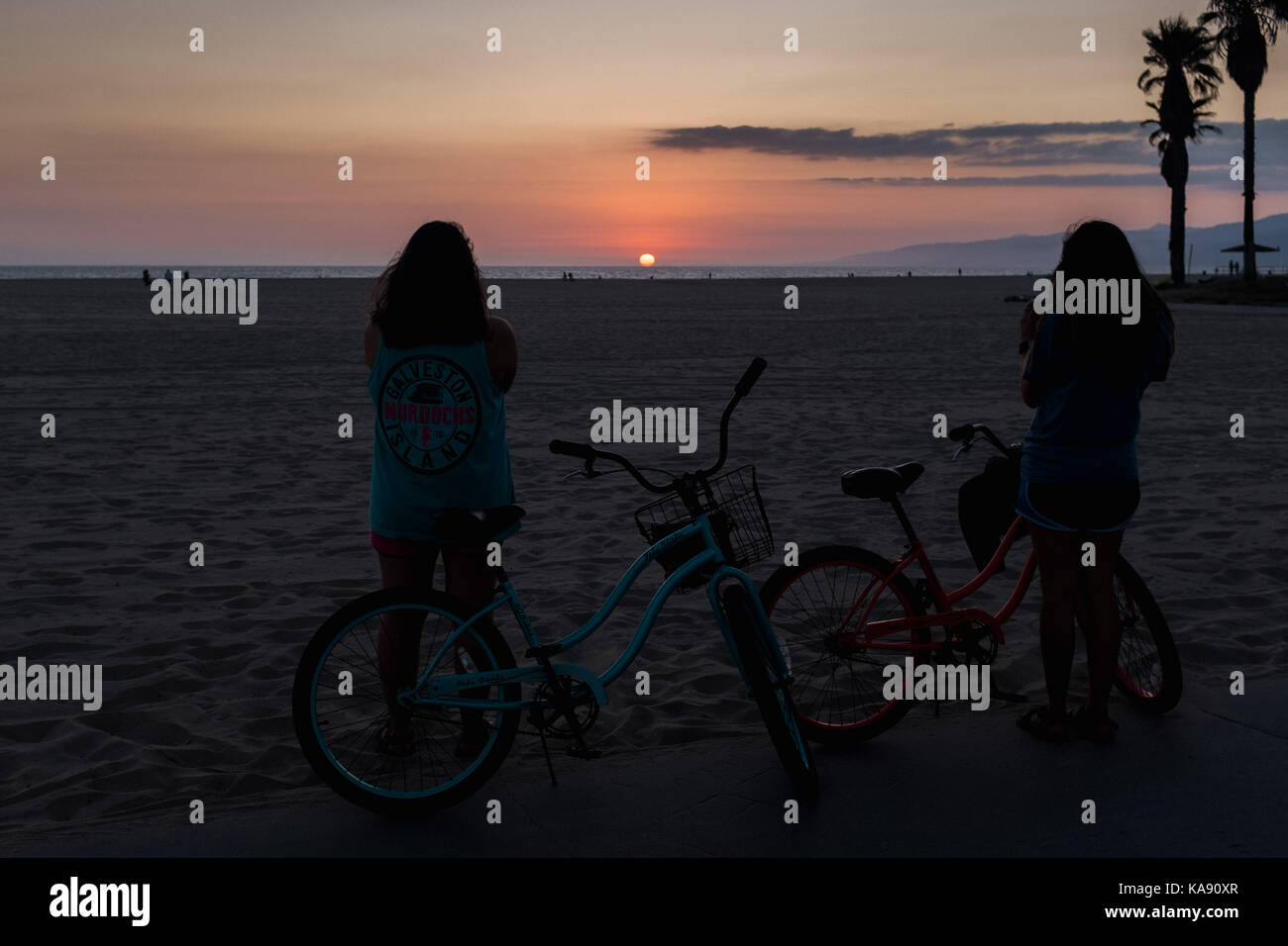Due ciclisti guardare il tramonto sulla spiaggia di Venice, Los Angeles, che si affacciano sull'Oceano Pacifico Foto Stock