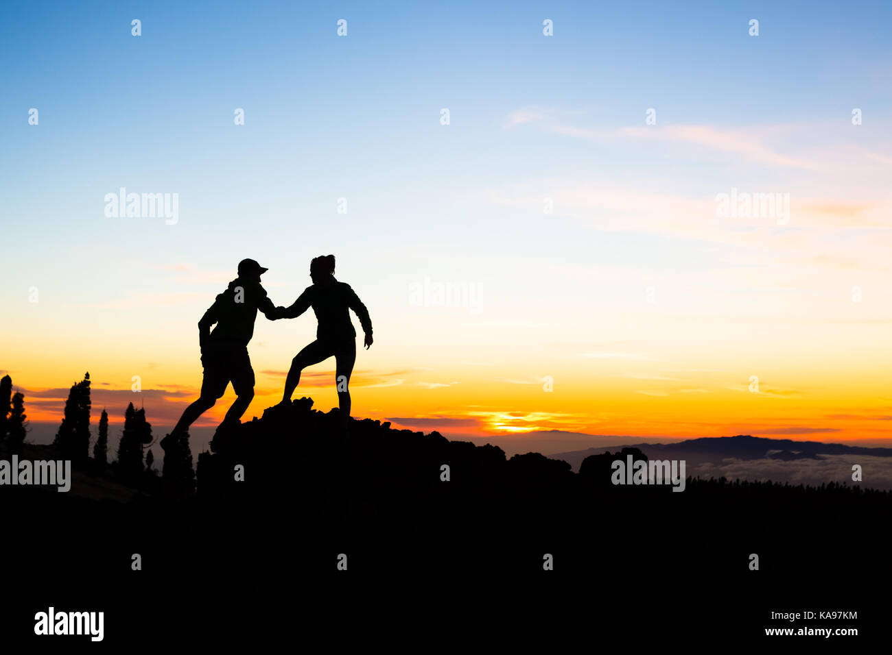 Il lavoro di squadra giovane con mano e fiducia. Silhouette della guida del team sulle montagne del tramonto. L uomo e la donna gli escursionisti o alpinisti il raggiungimento di obiettivi in inspira Foto Stock