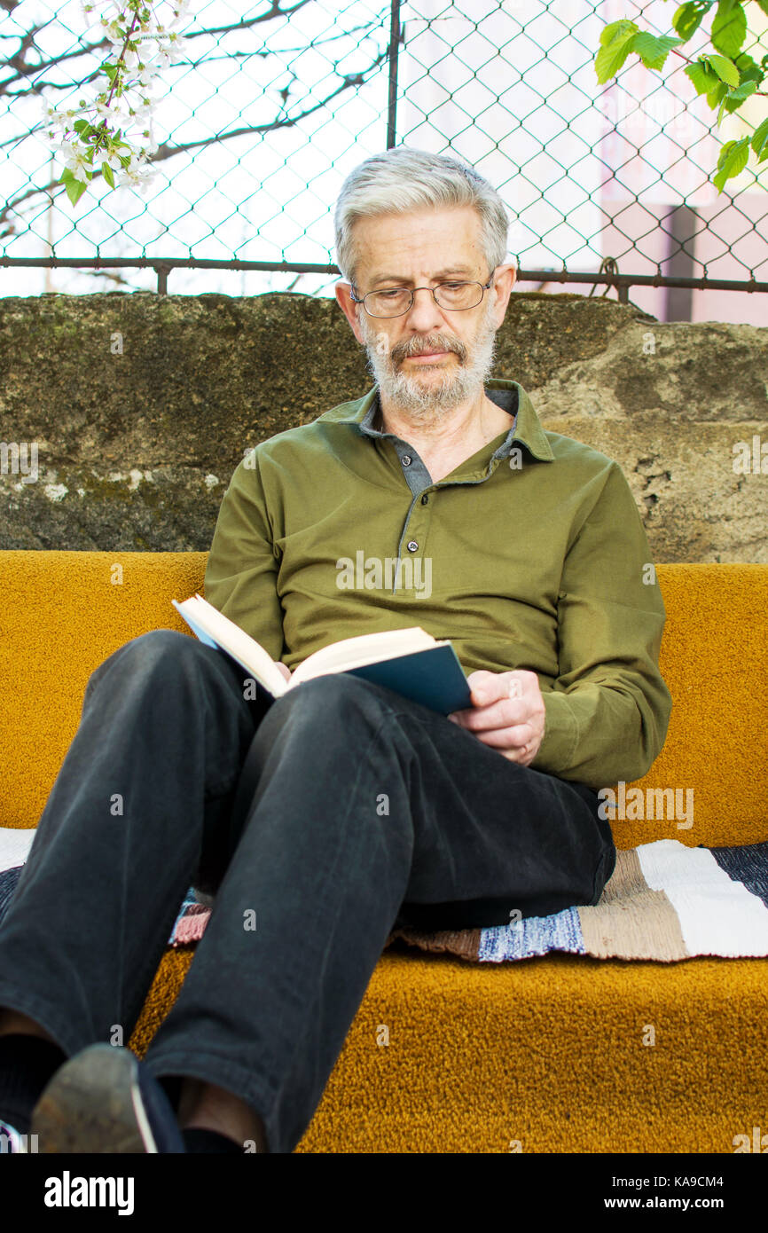 Senior uomo la lettura di un libro su un letto nel cortile posteriore Foto Stock