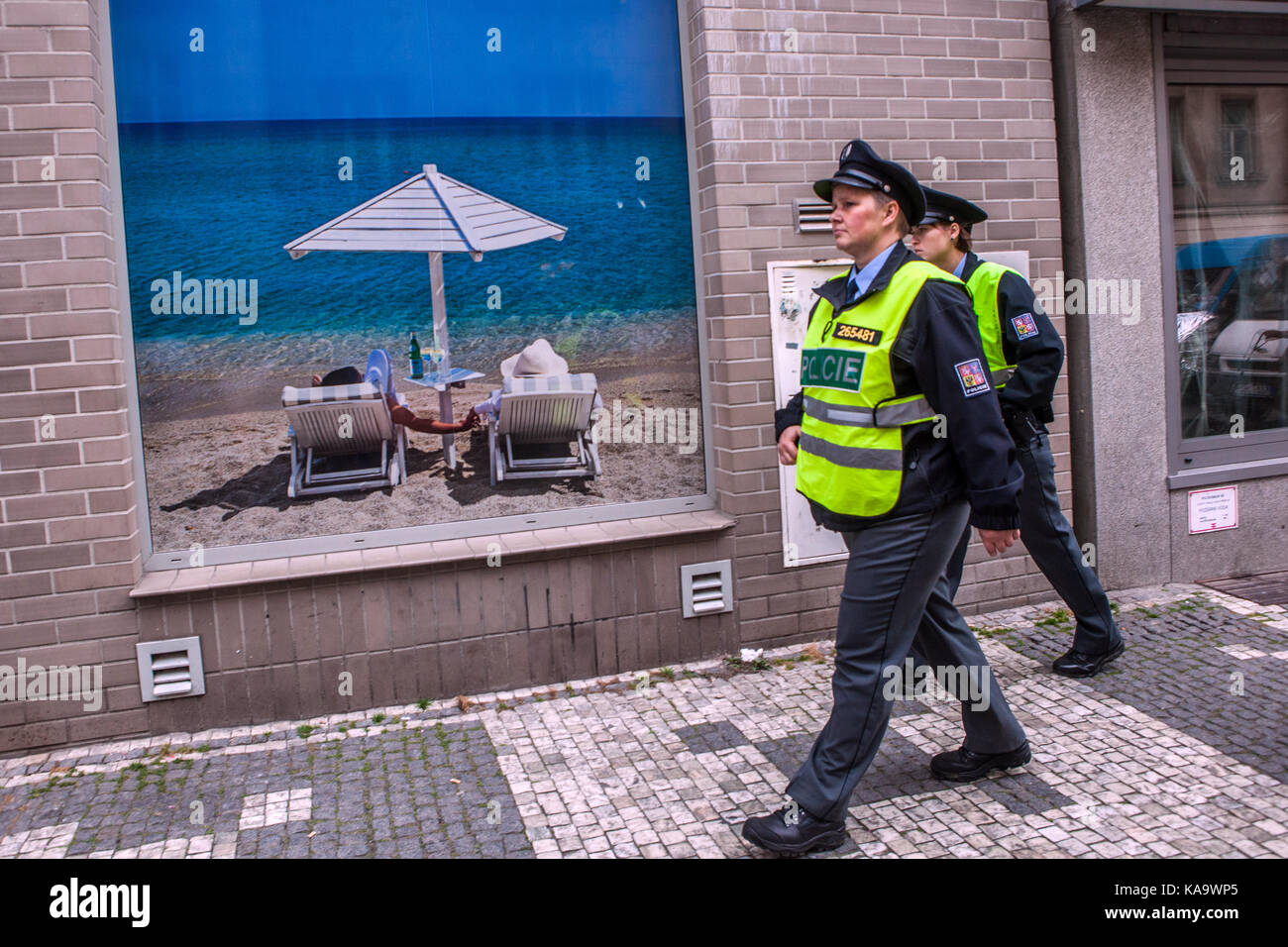 La polizia ceca pattuglia la strada, passa davanti a un poster per una vacanza fantastica in una vetrina di un negozio Praga Repubblica Ceca Foto Stock