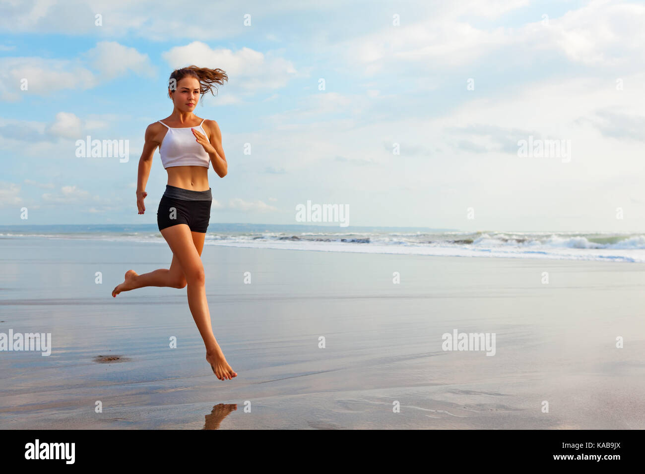 A piedi nudi ragazza sportiva con corpo sottile che corre lungo il mare surf da piscina di acqua per mantenere la forma e la salute. spiaggia con uno sfondo con cielo blu. donna fitness, fare jogging. Foto Stock