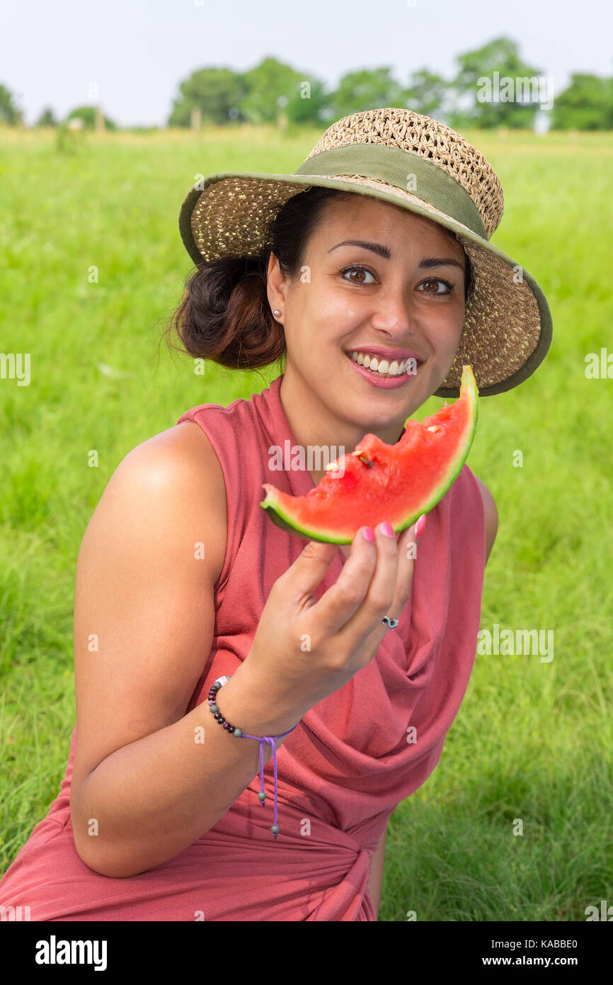 Giovane donna che indossa cappello di paglia mangiare fresco melone rosso nella natura Foto Stock